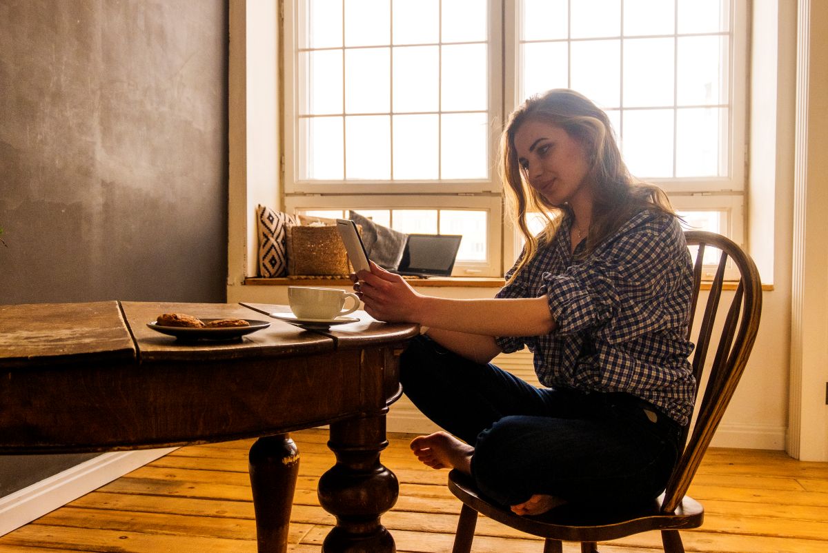 Kvinne ser på mobilen hjemme ved bordet og følger med på økonomien sin.