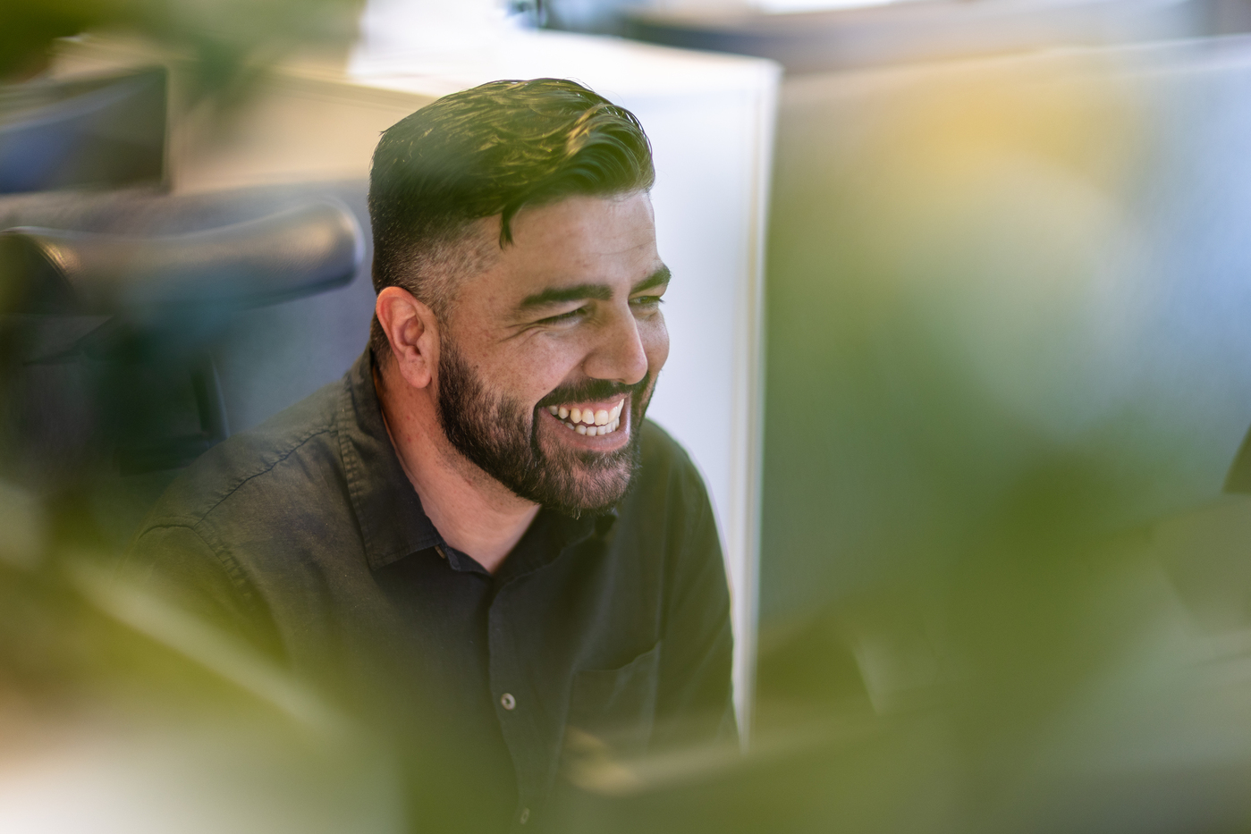 Smilende mann foran pc i et åpent kontorlandskap