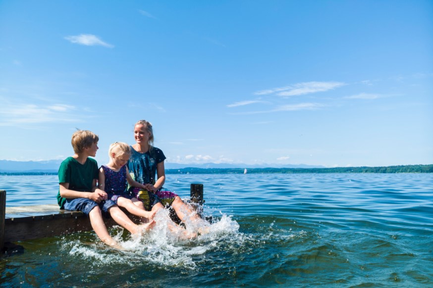 Familie sitter på en brygge og plasker beina i vannet